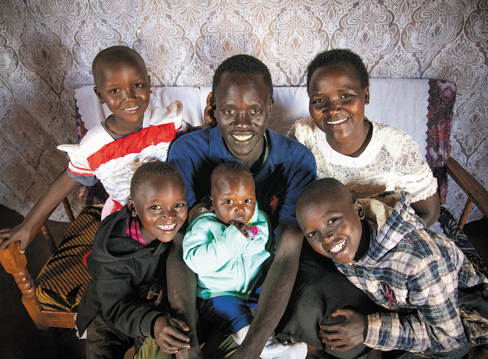 A man and his five children embrace on a couch, smiling for the camera.