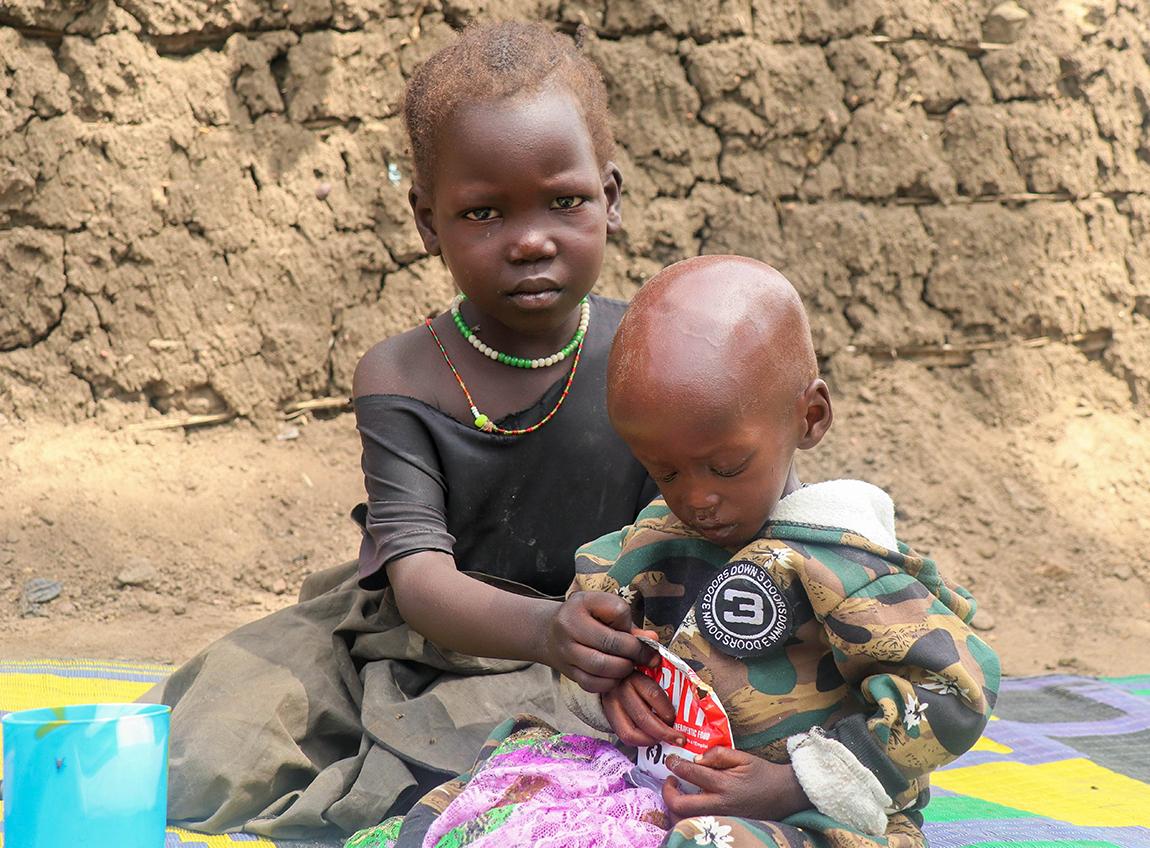 Two very young children in distress from hunger sit on the ground.
