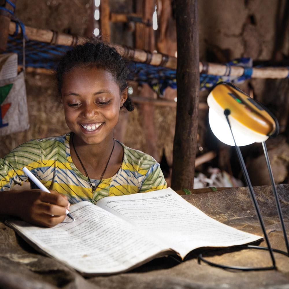 A solar light lights up a room as a young girl studies writing on a notebook.