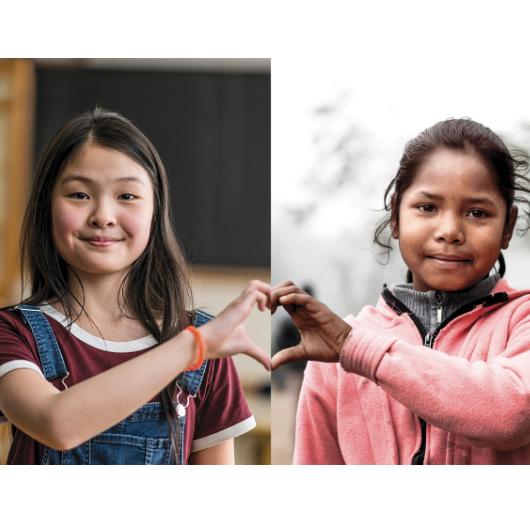 Two young girls join hands to form a heart.