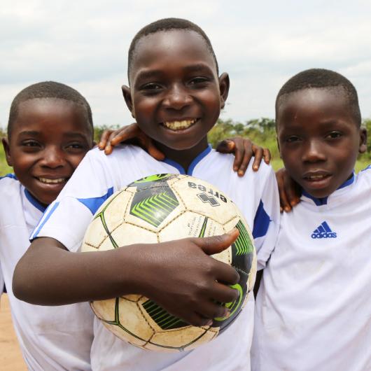 A young boy holding a soccer is embrace by two other young boys.