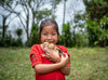 A little girl smiles as she holds up two baby chicks for the camera.