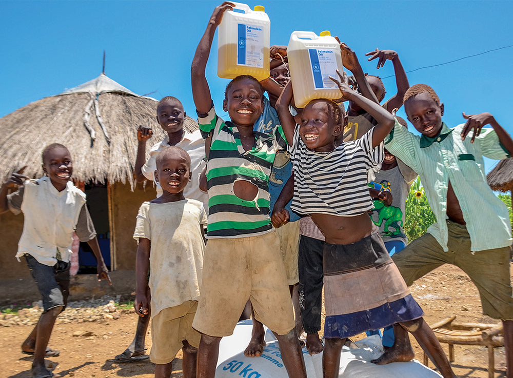 A group of eight smiling boys gathered around a pile of food donations.